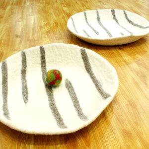 May include: Two white felt bowls with gray stripes. The bowl on the left has a small multi-colored ball inside.