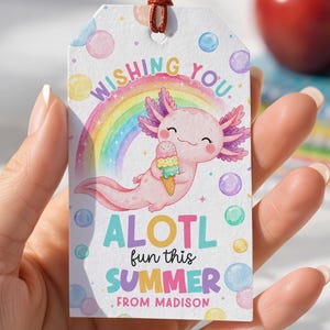 May include: A rectangular gift tag with a brown string, featuring a pink axolotl holding ice cream in front of a rainbow. The tag reads "Wishing you ALOTL fun this SUMMER. From Madison" with colorful bubble accents.