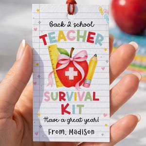 May include: A rectangular white gift tag with a lined paper pattern, featuring the text Back 2 school TEACHER SURVIVAL KIT Have a great year! From, Madison. The design includes a red apple with a white cross, a pink bow, a ruler, and a pencil.