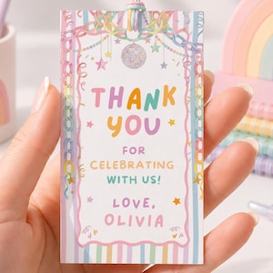 May include: A rectangular paper gift tag with a pastel rainbow border and confetti design. The text reads: THANK YOU FOR CELEBRATING WITH US! LOVE, OLIVIA. The tag features a small hole at the top with a thin, multicolored elastic string attached.