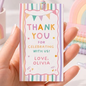 May include: A rectangular gift tag with a pastel striped border and a scalloped frame. The text reads: THANK YOU FOR CELEBRATING WITH US! LOVE, OLIVIA. The tag features colorful bunting, stars, and confetti graphics, and is attached to a pastel string.