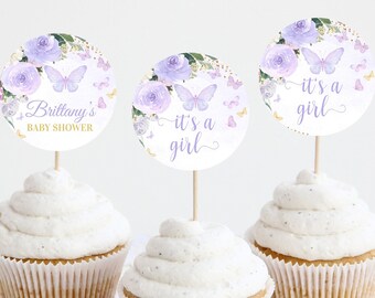 Könnte beinhalten: Drei violette und weiße Cupcake-Topper mit Schmetterlingen und Blumen. Die Topper sagen "It's a girl" und "Brittany's Baby Shower".