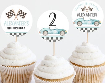 May include: Three cupcake toppers with a blue race car theme. The toppers feature a checkered flag, the number 2, and the text "Happy Birthday Alexander!"