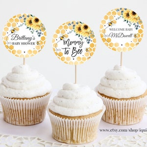 Puede incluir: Tres adornos para cupcakes amarillos y blancos con un patrón de panal, girasoles y abejas. Los adornos dicen "Mommy to Bee", "Brittany's Baby Shower" y "Welcome Baby McDowell".