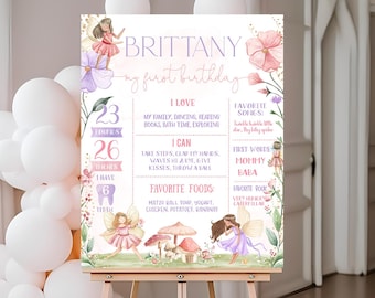 May include: A pink and purple first birthday sign featuring a fairy theme. The sign includes the name "Brittany", the age "1", and details about the child's favourite activities, foods, and words.