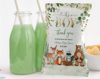 Op de afbeelding: Baby shower-cadeautasjes met een bos-thema. De tasjes zijn versierd met een groen en gouden ontwerp en bevatten een hert, een vos, een wasbeer en een beer. De tekst op het tasje luidt "It's a Boy" en "Bedankt voor het verwennen van onze baby met liefde." De datum van de baby shower staat ook op het tasje.