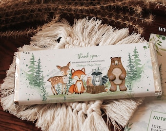 May include: A woodland-themed chocolate bar wrapper with a thank you message for attending a baby shower. The wrapper features a watercolor illustration of a deer, fox, raccoon, and bear in a forest setting. The text on the wrapper reads "Thank you for showering our baby with love. Brittany's Baby Shower."