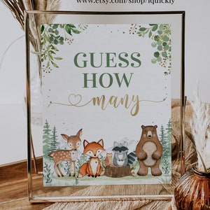 Op de afbeelding: Een printbaar bord met een bos-thema. Het bord zegt "Raad hoeveel" met een gouden hart en het woord "hoeveel" in gouden schrift. Het bord heeft een aquarel achtergrond met groene bladeren en verschillende bosdieren, waaronder een hert, een vos, een wasbeer, een uil en een beer.