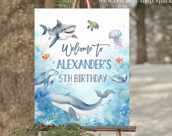 May include: A blue and white welcome sign with a watercolour background featuring sea creatures such as a shark, whale, dolphin, and jellyfish. The sign reads "Welcome to Alexander's 5th Birthday".