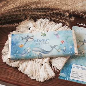 May include: A blue and white candy bar wrapper with an underwater scene featuring a whale, a shark, and a turtle. The wrapper says "Alexander's 5th Birthday".