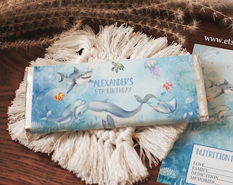 May include: A blue and white candy bar wrapper with an underwater scene featuring a whale, a shark, and a turtle. The wrapper says "Alexander's 5th Birthday".