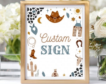 May include: A gold-framed sign with a white background and a blue and brown cowboy theme. The sign says "Custom Sign" and features illustrations of a cowboy hat, boots, cactus, and other western-themed imagery.
