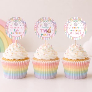 May include: Three cupcakes in rainbow-striped paper liners topped with white frosting and colorful sprinkles. Each cupcake features a round paper topper with pastel stripes, stars, and text reading Olivia's 2nd Birthday, Ready Two Party, and Happy Birthday Olivia.