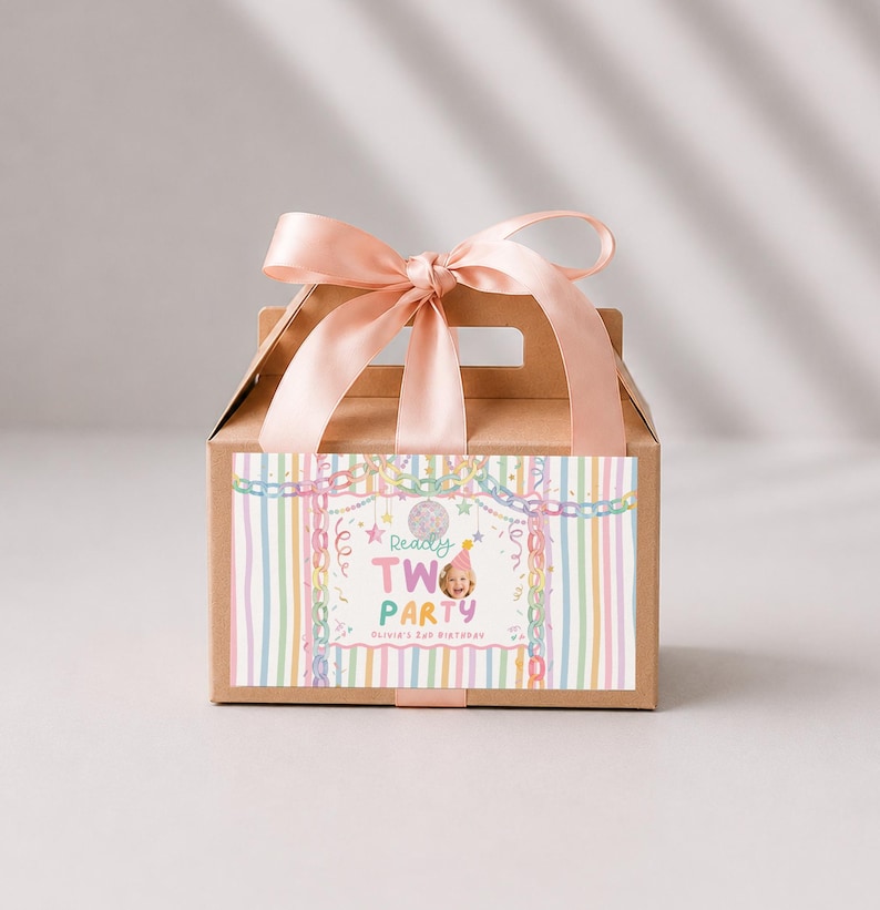 May include: A brown cardboard gable box with a light pink satin ribbon tied in a bow on top. The front features a label with pastel vertical stripes, a disco ball, and the text Ready TWO PARTY Olivia's 2nd Birthday with a photo of a child.