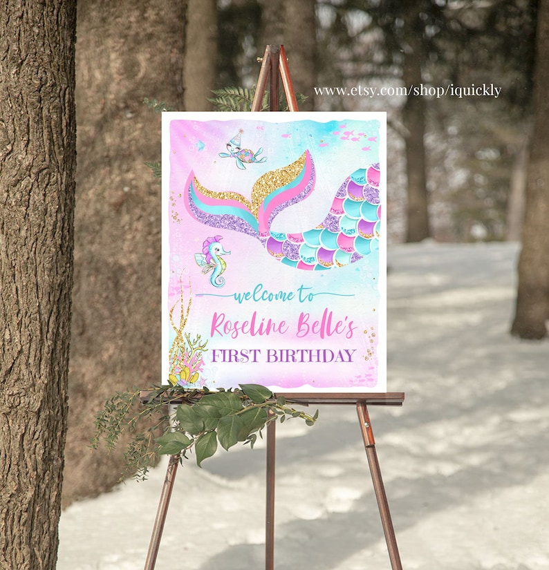 May include: A pink, blue and purple mermaid tail with gold glitter accents. The tail is on a welcome sign for a first birthday party. The sign says "Welcome to Roselina Belle's First Birthday".