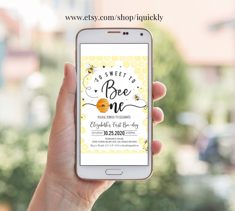 May include: A smartphone displaying a yellow and black bee-themed first birthday party invitation. The invitation reads "So Sweet to Bee One" and includes the date, time, and location of the party.