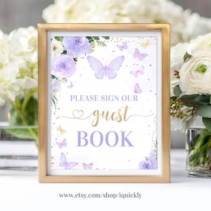 May include: Purple and gold guest book sign with a butterfly and floral design. The sign says "Please sign our guest book".