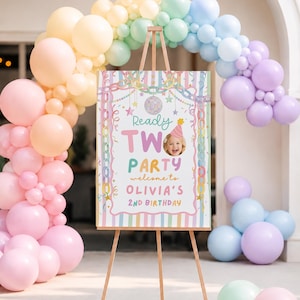 May include: A rectangular birthday sign on a wooden easel featuring pastel vertical stripes, a chain border, a disco ball, and the text Ready TWO PARTY welcome to OLIVIA'S 2ND BIRTHDAY with a photo of a child wearing a party hat, surrounded by balloons.