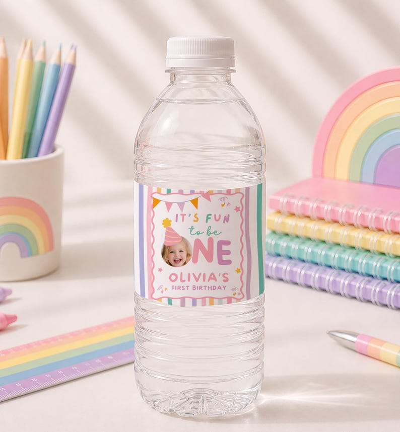 Pu&ograve; includere: Una bottiglia d'acqua in plastica trasparente con un'etichetta personalizzata che mostra la foto di un bambino con un cappellino da festa, strisce verticali colorate e il testo IT'S FUN to be ONE OLIVIA'S FIRST BIRTHDAY con stelline.