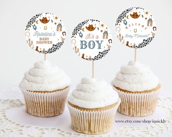 May include: Three cupcakes with white frosting topped with round paper cupcake toppers featuring a western baby shower theme. The toppers have a white background with black and brown illustrations of cacti, stars, horseshoes, cowboy boots, and a cowboy hat. The text on the toppers reads "Roseline's Baby Shower", "It's a Boy", and "Welcome Baby McDowall".