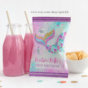 May include: Purple and blue mermaid tail party favour bags with gold glitter accents. The bags have a mermaid tail design with a seahorse and a starfish. The text on the bag reads "Roseline Belle's First Birthday!"