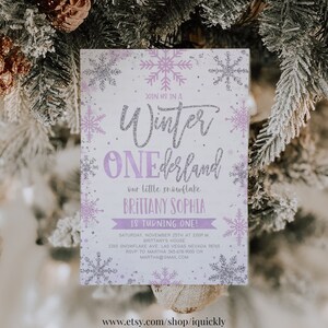 May include: A winter-themed invitation with a snowflake design. The invitation features the text "Winter ONEderland" in silver glitter, with the name "Brittany Sophia" and event details in purple. The background is white with purple and silver snowflakes.