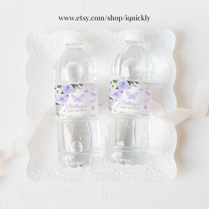 May include: Two clear plastic water bottles with purple and gold labels. The labels feature a floral design with butterflies and the text "Brittany's Baby Shower".