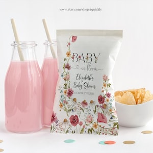 May include: A baby shower setup featuring pink drinks in glass bottles with straws, a white bag with floral design and text, and a bowl of chips. The bag reads "Baby in Bloom" and "Elizabeth's Baby Shower October 25th 2024."