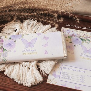 May include: A white chocolate bar wrapper with a purple butterfly and floral design. The wrapper says "Brittany's Baby Shower".