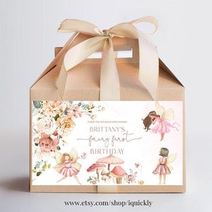 May include: A brown favor box with a pink and white floral design and a label that says "Thank you so much for coming! Brittany's Fairy First Birthday". The box is tied with a beige ribbon.