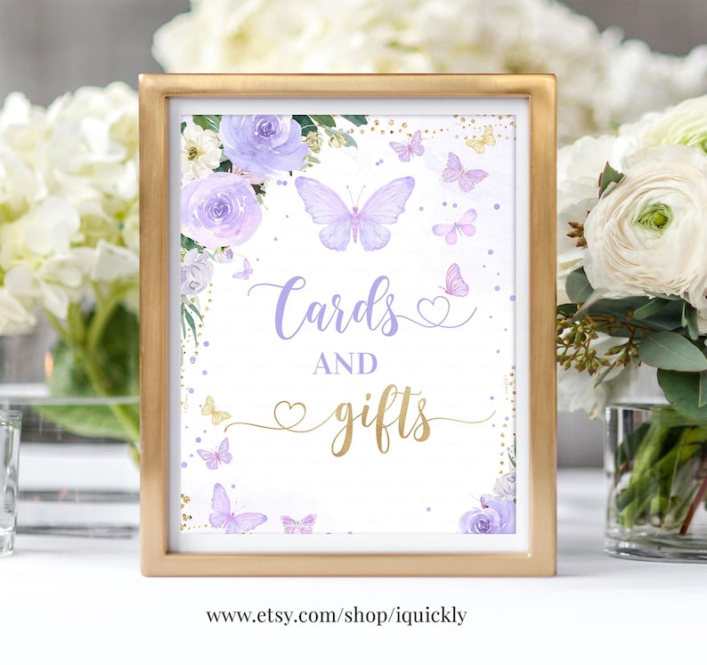 May include: A purple and gold sign with a floral design and butterflies. The sign says "Cards and gifts" with a heart symbol. The text at the bottom of the sign says "www.etsy.com/shop/iquickly".