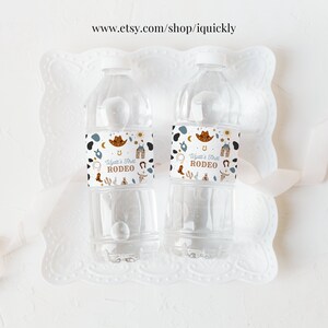 May include: Two clear plastic water bottles with white labels. The labels have a western theme with a cowboy hat, horseshoe, and the text "Wyatt's First Rodeo".
