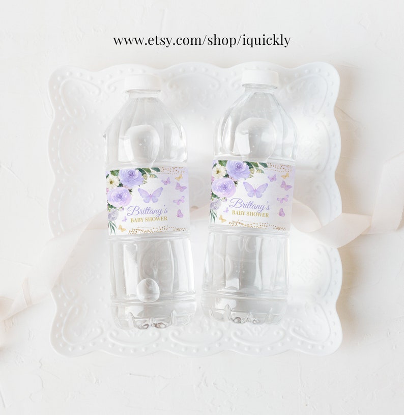 May include: Two clear plastic water bottles with purple and gold labels. The labels feature a floral design with butterflies and the text "Brittany's Baby Shower".