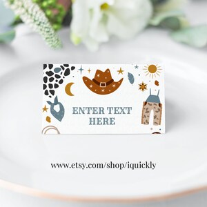May include: A white card with a cowboy hat, stars, a sun, and a pair of overalls printed on it. The text "ENTER TEXT HERE" is printed in black on the card. The card is on a white plate.