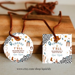 May include: Two round and square thank you tags with a western theme. The tags are white with black and white animal print, blue and orange accents, and illustrations of a cowboy hat, boots, a horseshoe, a cactus, and a lasso. The text on the tags reads "Thanks Y'all for galloping on by to celebrate my first rodeo. Love, Wyatt."