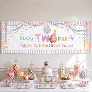 May include: A rectangular birthday banner featuring pastel stripes, a disco ball, and the text Ready TWO PARTY HAPPY 2ND BIRTHDAY OLIVIA with a photo of a child. Below, a table displays a tiered cake, glass jars of colorful candies, and cupcakes.