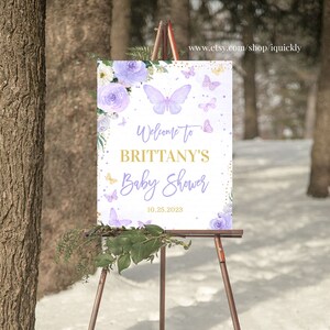 May include: Purple and gold baby shower welcome sign with butterflies and flowers. The sign says "Welcome to Brittany's Baby Shower 10.25.2023".
