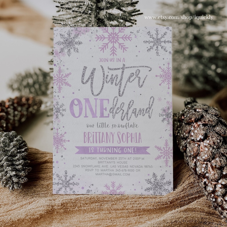 May include: A winter-themed invitation with a snowflake design. The invitation features the text "Winter ONEderland" in silver glitter and lavender. The invitation includes the name "Brittany Sophia" and event details. The invitation is surrounded by silver and lavender snowflakes.