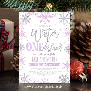May include: A Winter ONEderland invitation with a snowflake theme. The invitation features the text "Winter ONEderland" in silver glitter, with the name "BRITTANY SOPHIA" and the words "IS TURNING ONE!" in purple. The invitation also includes event details.