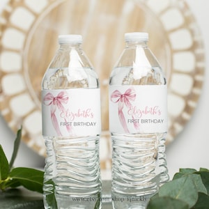 May include: Two clear plastic water bottles with white labels. The labels feature a pink watercolour bow and the text "Elizabeth's First Birthday".