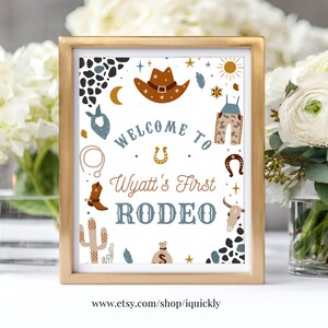 May include: A white sign with a gold frame, announcing "Welcome to Wyatt's First Rodeo". The sign is decorated with cowboy hats, boots, and other western-themed imagery in blue, brown, and gold.