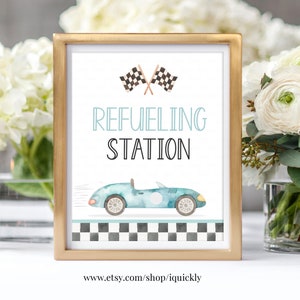 Puede incluir: Un cartel imprimible con un marco dorado, que presenta un coche de carreras azul con un fondo de bandera a cuadros. El cartel dice "Estación de repostaje" e incluye el sitio web www.etsy.com/shop/iquickly.