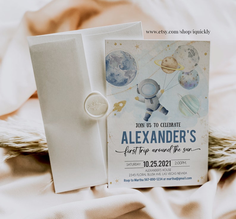 May include: A blue and white invitation card with a watercolor illustration of an astronaut holding balloons shaped like planets. The text on the card reads "Join us to celebrate Alexander's first trip around the sun" and includes the date and time of the event.