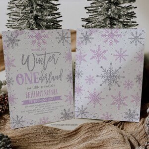 May include: A two-sided invitation with a winter theme. The front features the text "Winter ONEdrland" with snowflake accents in silver and lavender. The back has a pattern of snowflakes. The invitation is for Brittany Sophia's first birthday.