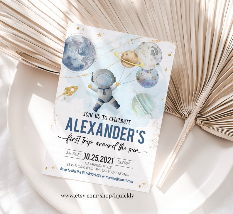 May include: A blue and white invitation with gold glitter accents. It features an astronaut holding balloons shaped like planets. The text reads "Join us to celebrate Alexander's first trip around the sun. Saturday 10.25.2021 2:00PM Alexander's House 2345 Floral Blush Ave Las Vegas Nevada Rsvp to Martha 567-890-1234 or martha@gmail.com www.etsy.com/shop/iquickly"