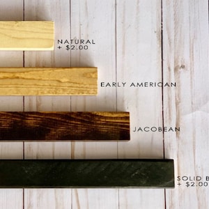 May include: Four wood samples in different colors: natural, early American, Jacobean, and solid black. The text "NATURAL + $2.00" is written below the first sample. The text "EARLY AMERICAN" is written below the second sample. The text "JACOBBEAN" is written below the third sample. The text "SOLID BLACK + $2.00" is written below the fourth sample.