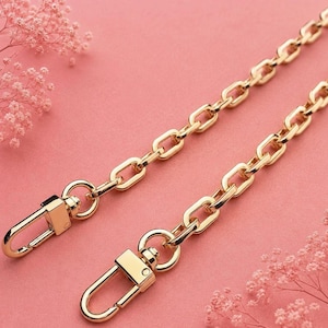 May include: A gold-toned metal chain strap featuring rectangular links and two swivel lobster claw clasps at the ends. The chain has a polished finish and is designed for attaching to bags or accessories, providing a secure and functional connection.