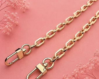 May include: A gold-toned metal chain strap featuring rectangular links and two swivel lobster claw clasps at the ends. The chain has a polished finish and is designed for attaching to bags or accessories, providing a secure and functional connection.