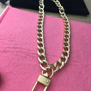 May include: A gold chain necklace with a gold clasp. The chain is a thick, curb style chain.