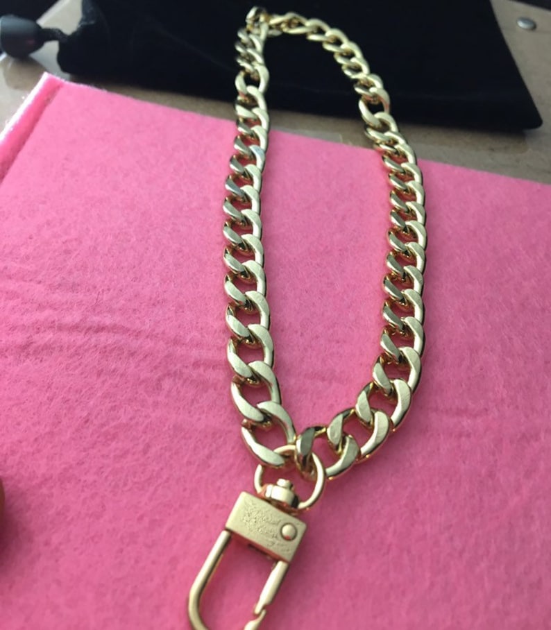 May include: A gold chain necklace with a gold clasp. The chain is a thick, curb style chain.